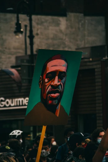 a person holding a sign with a picture of a man on it, by Andrew Stevovich, pexels contest winner, black arts movement, lebron james, pastel artwork, green skinned, kanye west