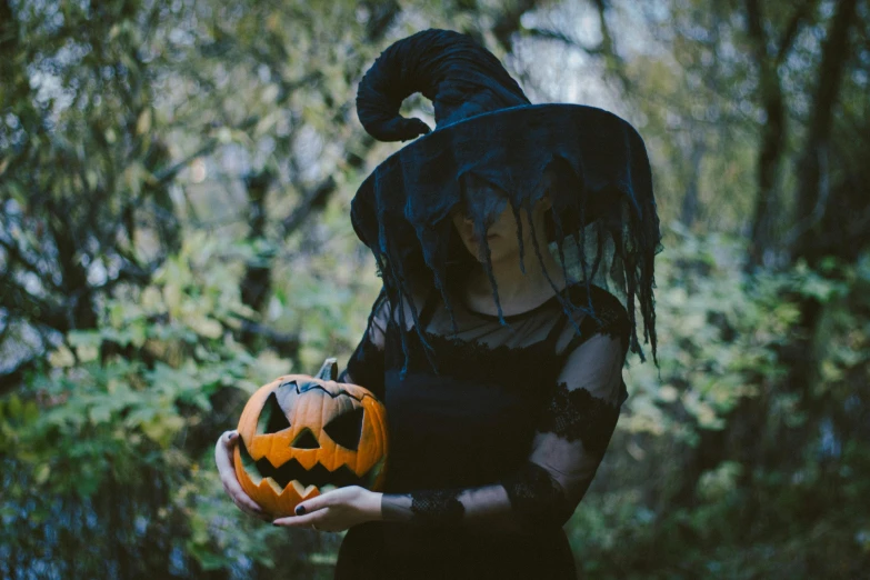 a woman in a witch costume holding a pumpkin, pexels, surrealism, black hat, still photograph, black, a handsome