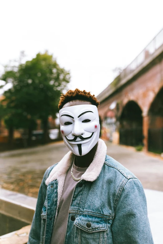 a man wearing a guy mask standing on a bridge, trending on pexels, antipodeans, donald glover, non-binary, 💣 💥💣 💥, white facepaint