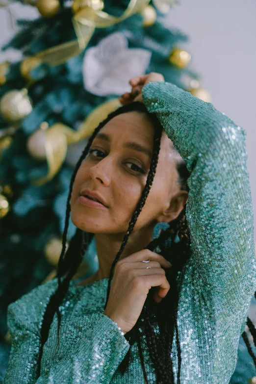 a woman standing in front of a christmas tree, an album cover, trending on pexels, ashteroth, long braided teal hair, portrait sophie mudd, shiny and sparkling