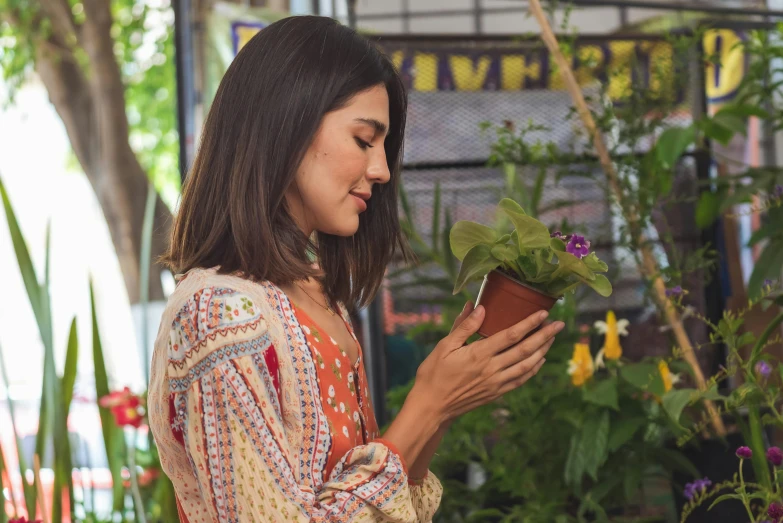 a woman looking at a plant in a pot, pexels contest winner, arts and crafts movement, middle eastern style vendors, handsome girl, dua lipa, in garden