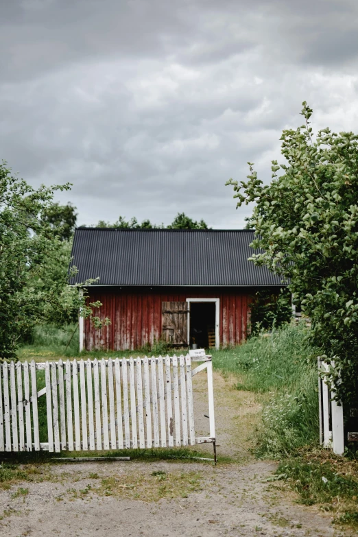 a white gate in front of a red barn, by Jesper Myrfors, unsplash, modernism, low quality photo, with fruit trees, old cabin, buildings covered in black tar