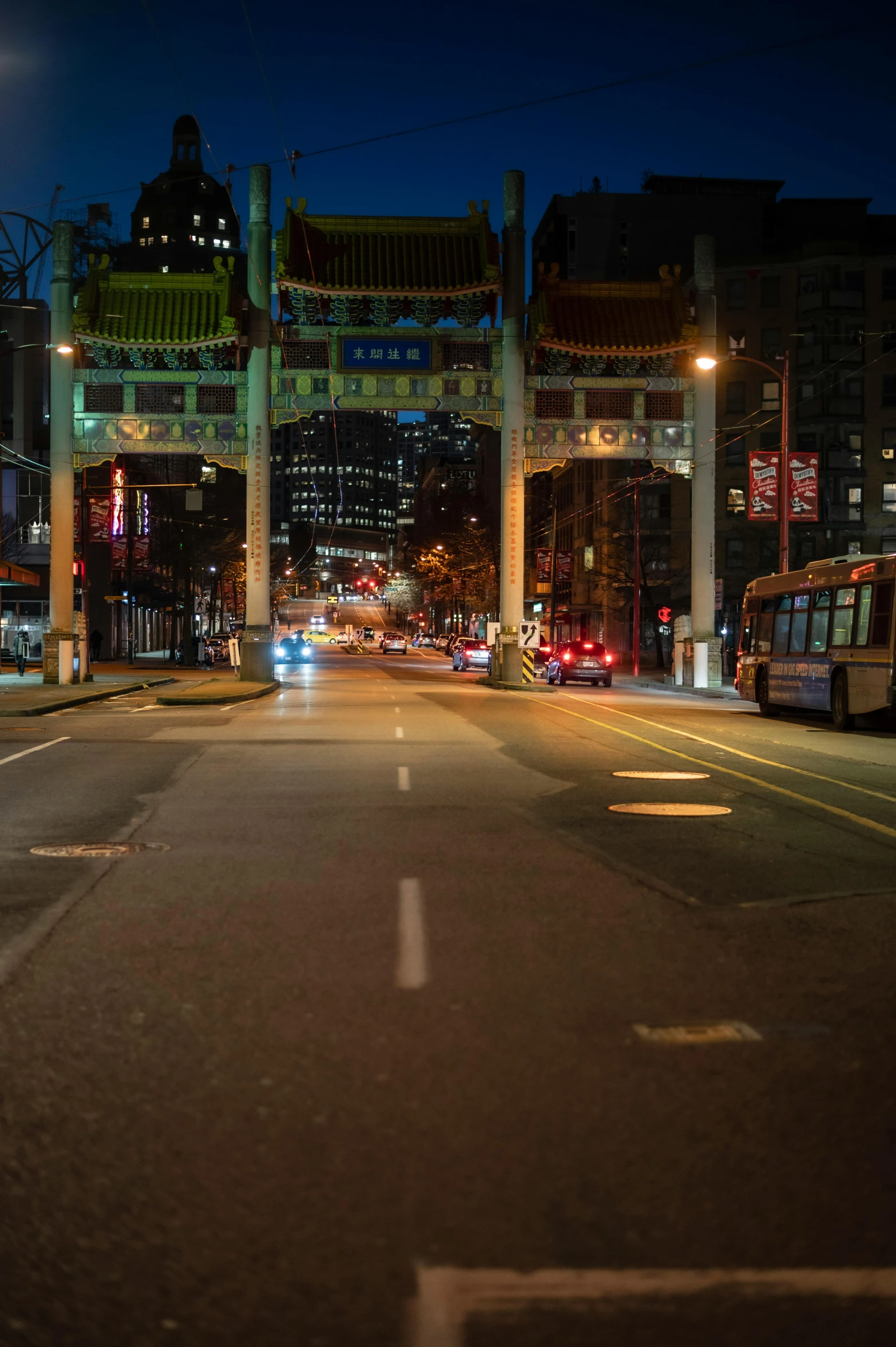 a city street filled with lots of traffic at night, on a sidewalk of vancouver, archway, empty streets, street signs