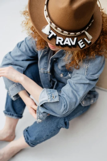 a woman sitting on the floor wearing a hat, by Nina Hamnett, trending on pexels, wearing a jeans jackets, promotional image, conde nast traveler photo, kids