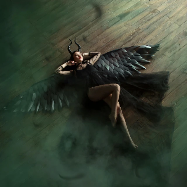 a woman in a black dress laying on a wooden floor, an album cover, by Gavin Nolan, trending on cgsociety, conceptual art, has black wings, still from loki ( 2 0 2 1 ), photography alexey gurylev, female disney villain