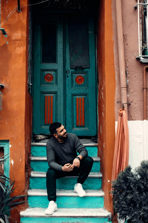 a man sitting on the steps of a building, a colorized photo, pexels contest winner, turquoise and venetian red, door, a portrait of rahul kohli, teal orange color palette 8k