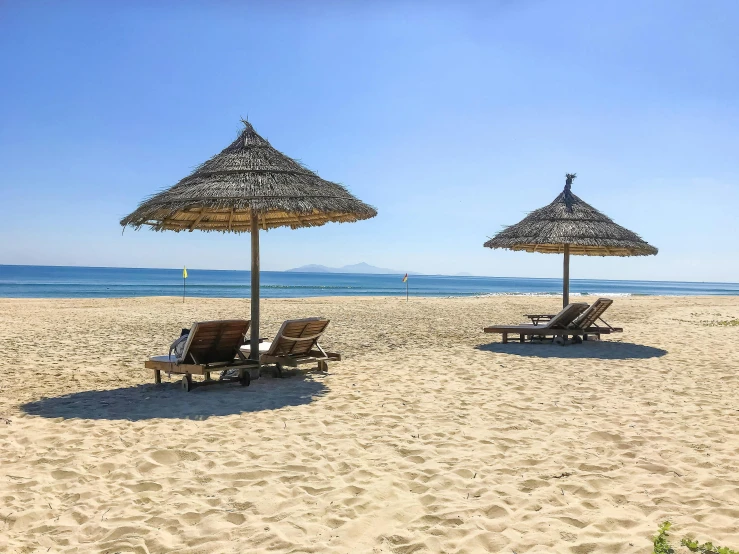 a couple of lounge chairs sitting on top of a sandy beach, vietnam, profile image, parasols, square