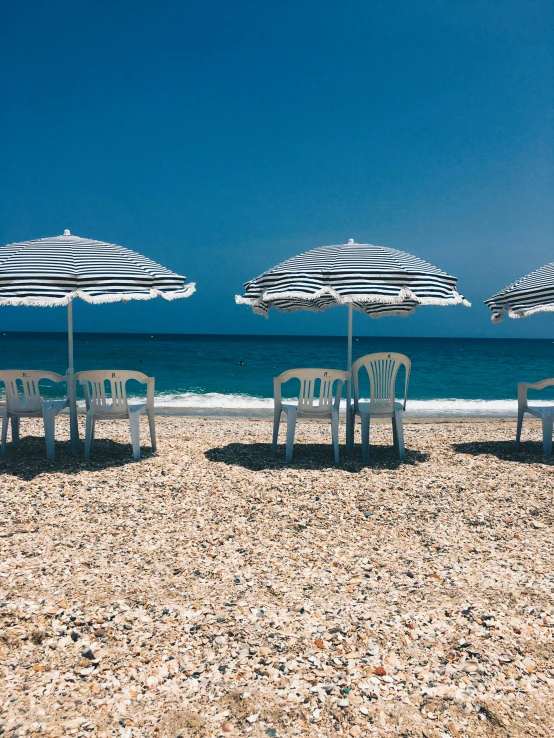 a number of chairs and umbrellas on a beach, unsplash contest winner, black sea, striped, album cover, profile image