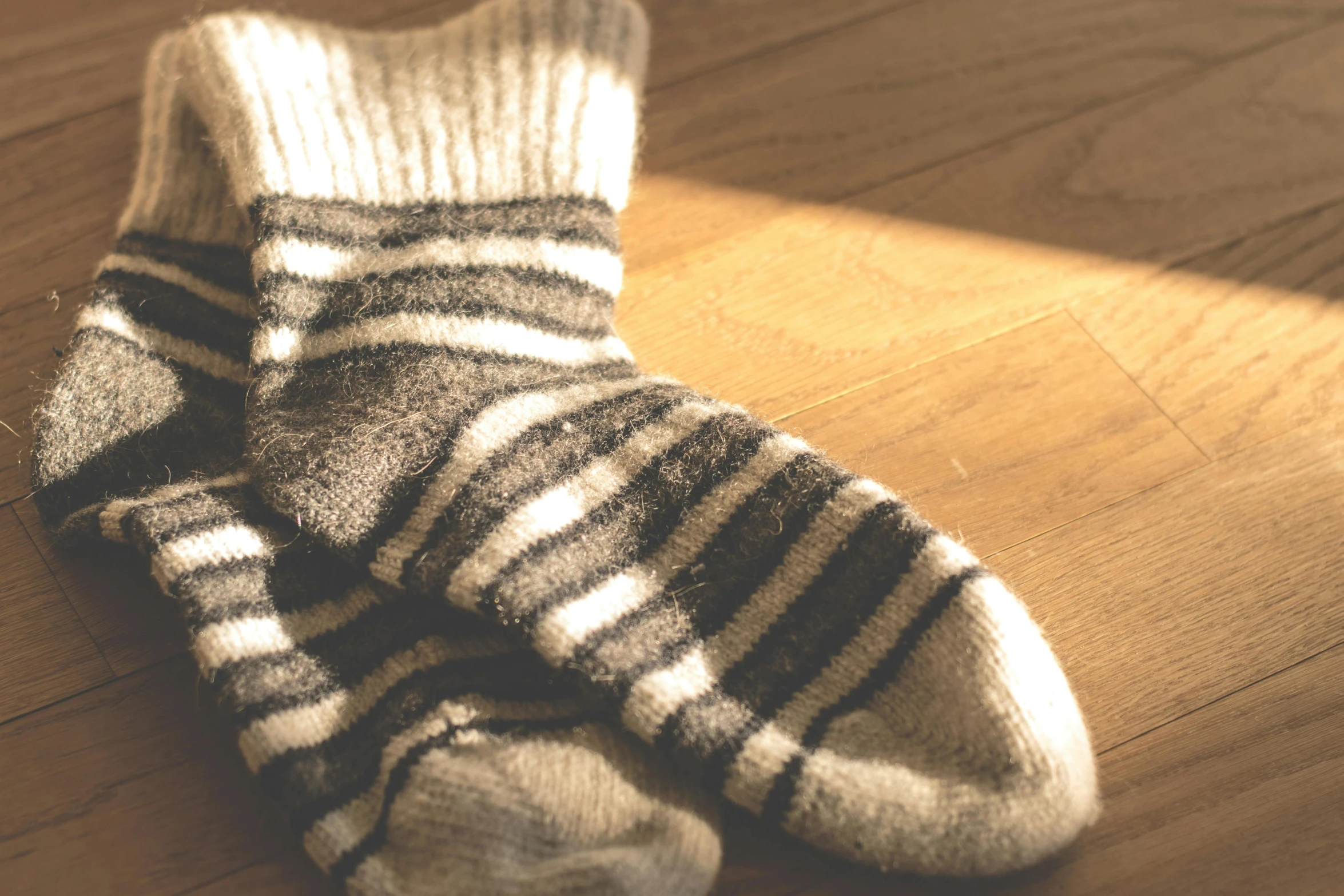 a pair of socks sitting on top of a wooden floor, unsplash, sepia sunshine, striped, soft and fluffy, warmly lit
