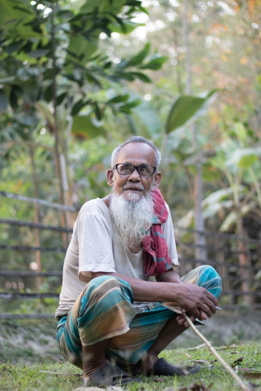 a man sitting on the ground next to a cow, a portrait, inspired by Sunil Das, hurufiyya, amongst foliage, overalls and a white beard, bangladesh, slide show