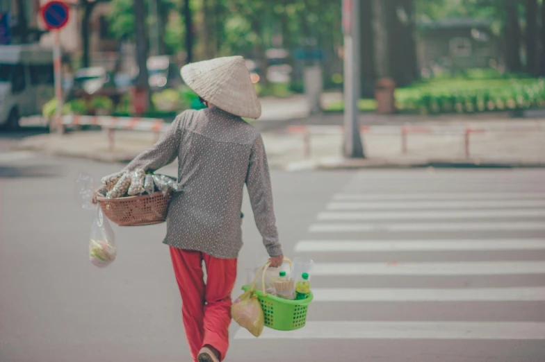 a woman walking across a street with a basket of food, pexels contest winner, dang my linh, avatar image, sustainable materials, baggy clothing and hat