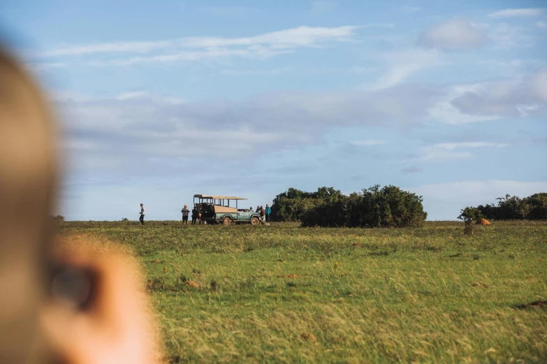 a person taking a picture of a tractor in a field, by Peter Churcher, pexels contest winner, standing in the savannah, view from a distance, people resting on the grass, looking onto the horizon