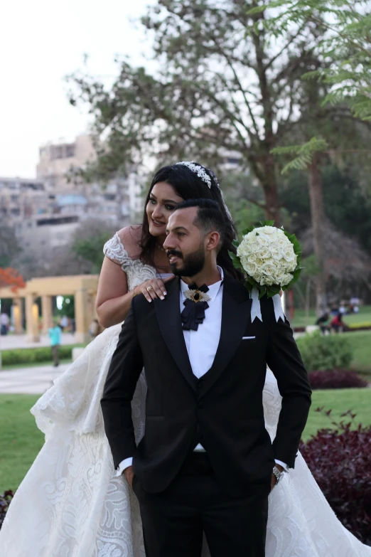 a man in a tuxedo and a woman in a wedding dress, by Ahmed Yacoubi, happening, with a park in the back ground, smiling couple, bouquet, elaborate hair worn up