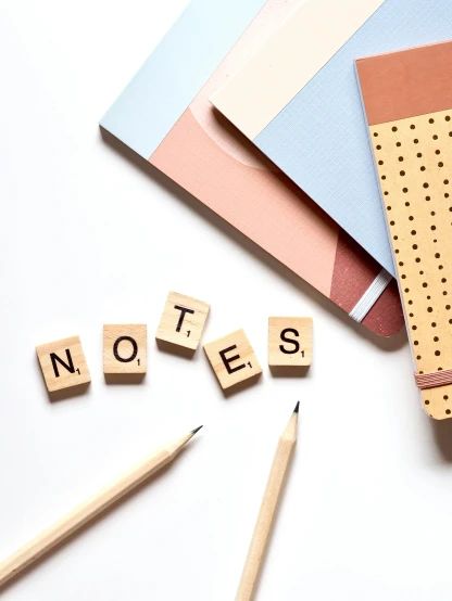 a note book sitting on top of a table next to a pencil, by Robbie Trevino, letterism, building blocks, close-up product photo, square shapes, beige