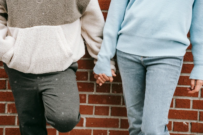 a man and a woman holding hands in front of a brick wall, a colorized photo, trending on pexels, happening, background image, thigh gap, cozy aesthetic, soft and fluffy