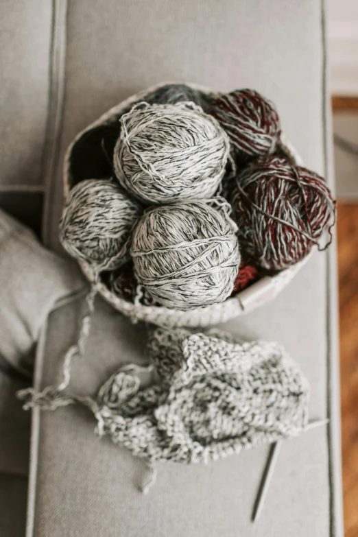 a bowl filled with yarn sitting on top of a couch, by Jessie Algie, unsplash, grey and silver, scattered props, bulky build, silver red white details