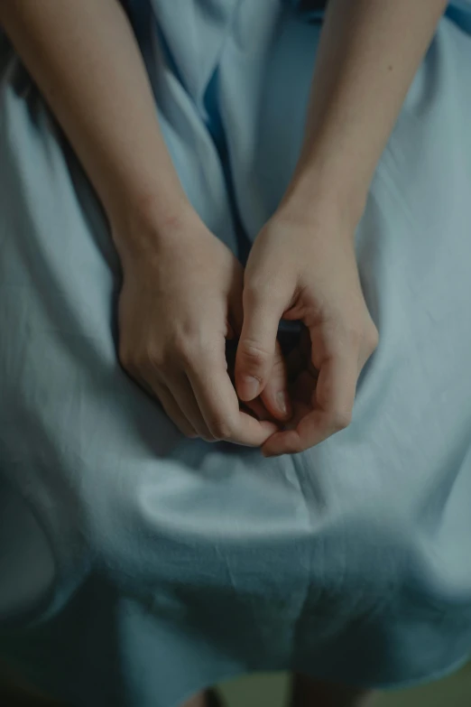 a woman in a blue dress holding her hands, by Elsa Bleda, trending on reddit, wearing a hospital gown, 4 k film still, curled up under the covers, color graded