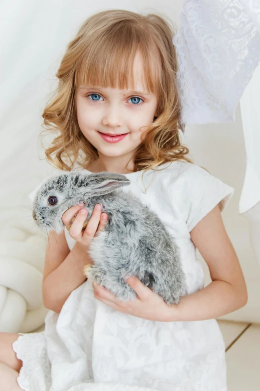 a little girl sitting on a couch holding a stuffed rabbit, inspired by Sophie Anderson, shutterstock contest winner, renaissance, pure grey fur, on a white table, softplay, a blond