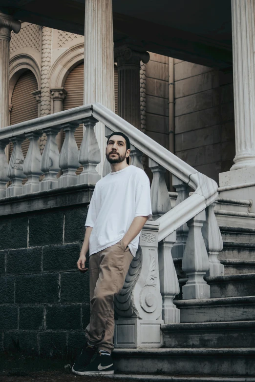 a man standing on the steps of a building, an album cover, inspired by Camilo Egas, pexels contest winner, dressed in a white t-shirt, looking to the side off camera, chilean, neo - classical