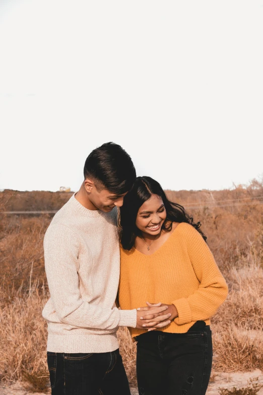 a man and woman standing next to each other in a field, a picture, trending on unsplash, happening, pregnant belly, warm color clothes, turning her head and smiling, yellow