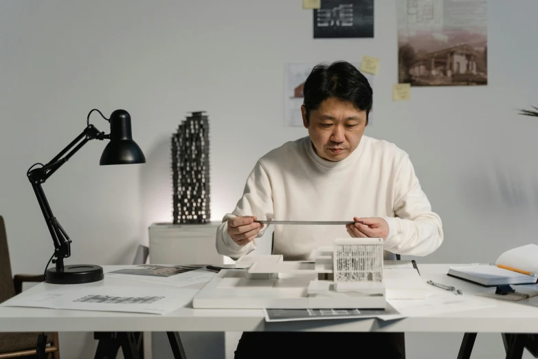 a man sitting at a table working on a model, inspired by Joong Keun Lee, pexels contest winner, dezeen showroom, light source from the left, nishimiya shouko, an architectural