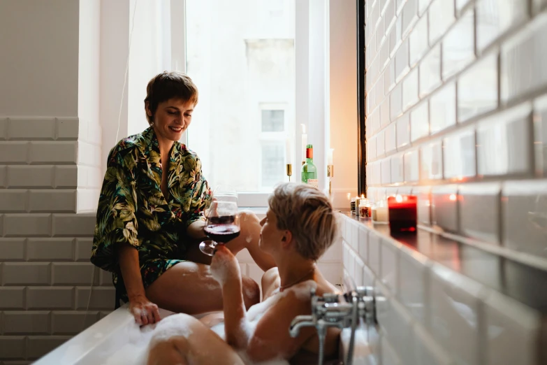 a woman and a child sitting in a bathtub, by Julia Pishtar, pexels contest winner, enjoying a glass of wine, non binary model, lesbians, couple on bed