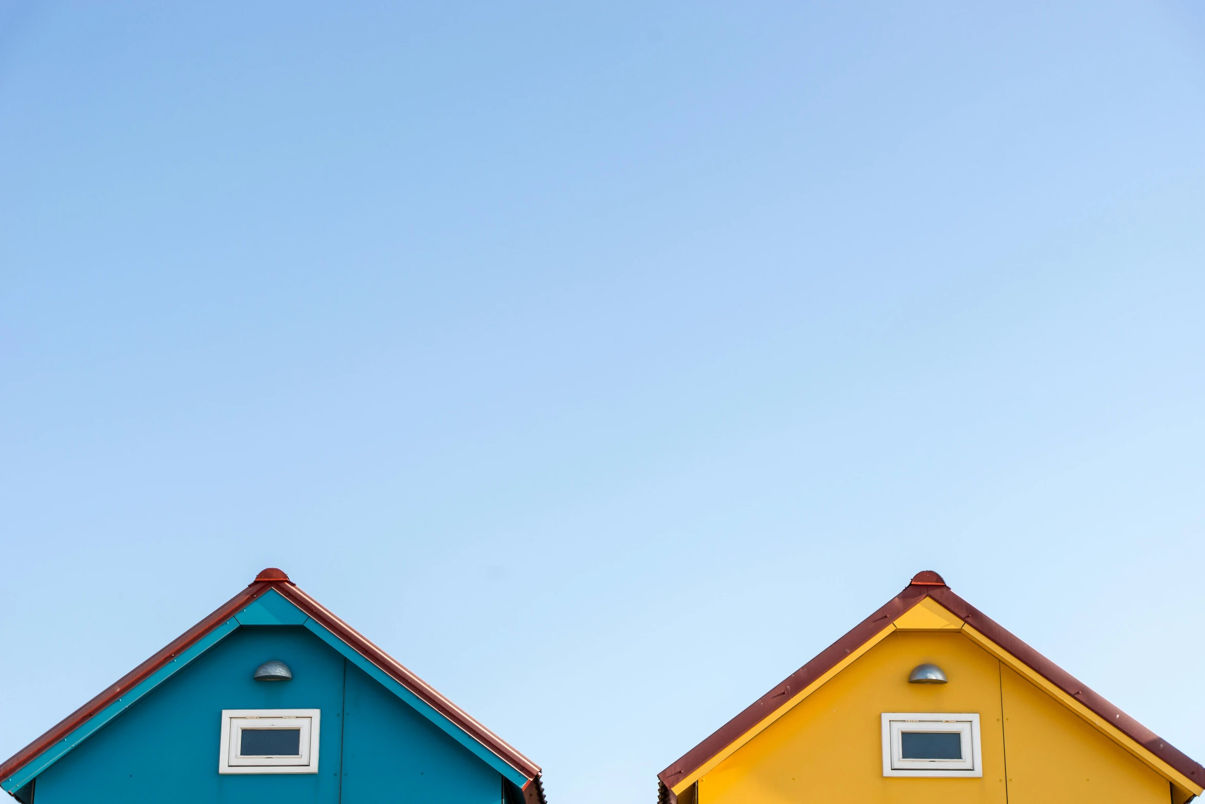 a couple of colorful houses sitting next to each other, a picture, pexels contest winner, minimalism, summer clear blue sky, shed roof, blue and yellow lighting, tiny house