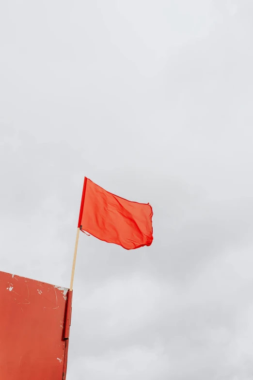 a man standing on top of a beach next to a red flag, pexels, symbolism, square, orange, on a gray background, shot from below