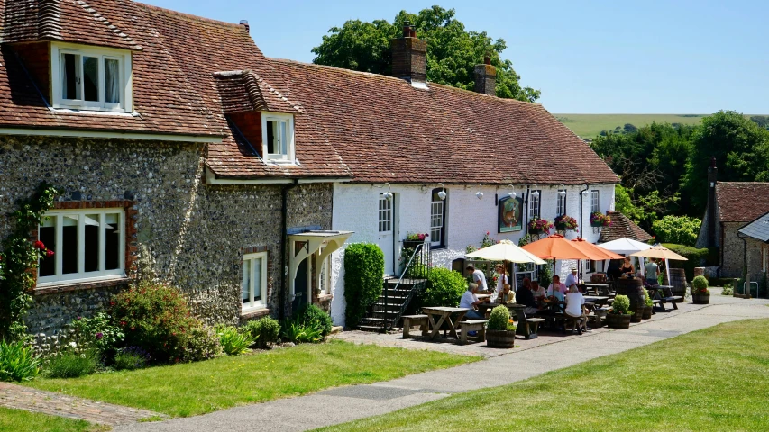 a group of people sitting outside of a building, inspired by George Lambourn, pexels, idyllic cottage, restaurant, white buildings with red roofs, madgwick