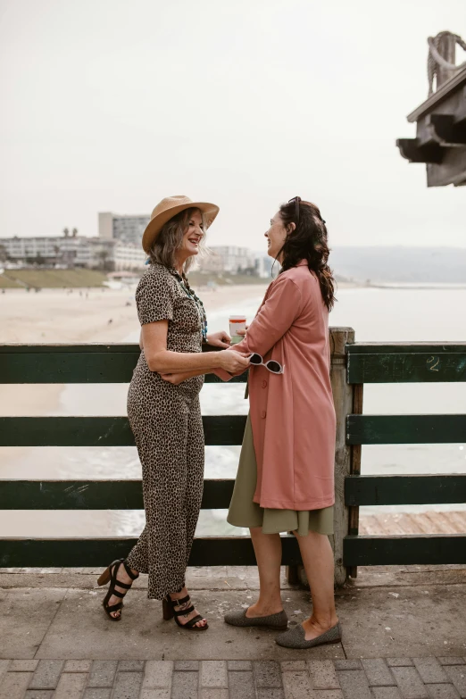 two women standing next to each other on a pier, unsplash, renaissance, overlooking the beach, wearing a french beret, wearing a colorful men's suit, muted browns