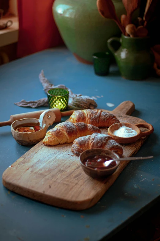 a wooden cutting board topped with croissants, a still life, inspired by Charles Le Roux, renaissance, moroccan, medium - shot, lights, patagonian