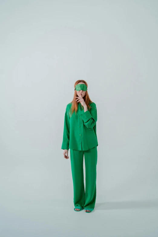 a woman in a green suit talking on a cell phone, an album cover, by Anita Malfatti, trending on pexels, blindfold, in a white room, ( redhead, wearing pajamas