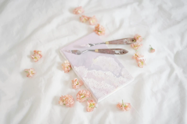 a book sitting on top of a bed covered in flowers, pastel pink concrete, cutlery, detailed product image, pair of keycards on table