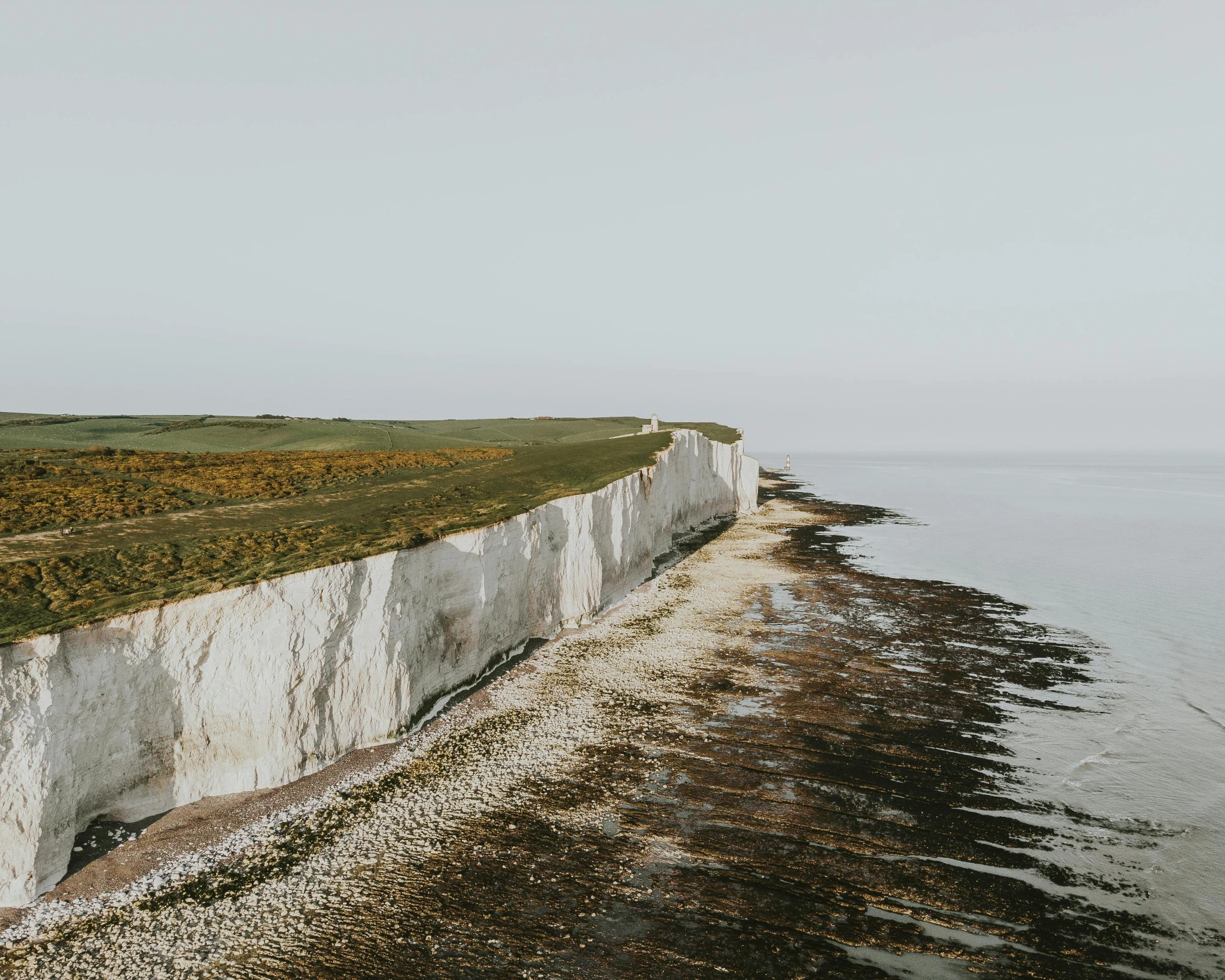 a man standing on top of a cliff next to the ocean, by Daniel Seghers, pexels contest winner, chalk cliffs above, an expansive grassy plain, aerial footage, united kingdom