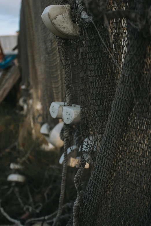 a close up of a fishing net with a boat in the background, unsplash, graffiti, bells, grey, evening lighting, - 9