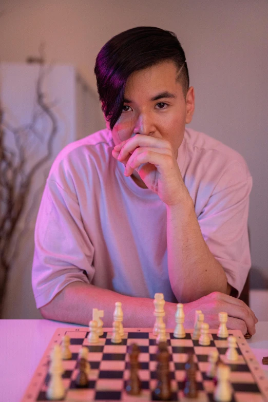 a man sitting at a table with a chess board, an epic non - binary model, gemma chen, profile image, tournament