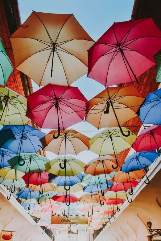 a bunch of umbrellas hanging from the ceiling of a building, brightly colored buildings, highly upvoted, covered