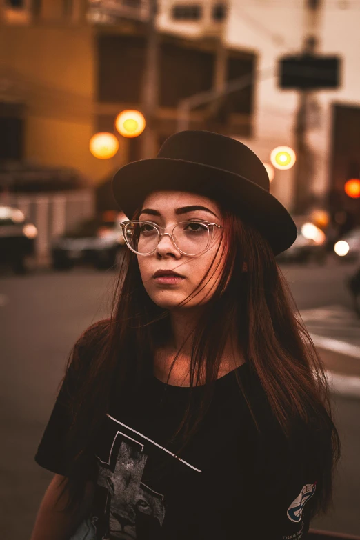 a woman with glasses and a hat on a city street, a picture, inspired by Elsa Bleda, trending on pexels, androgynous face, low lights, square glasses, portrait of vanessa morgan