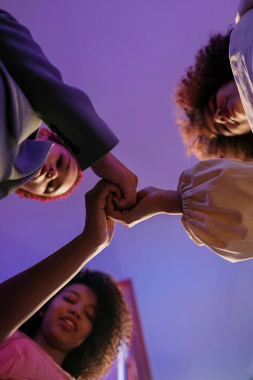 a group of people holding hands in a circle, black arts movement, brightly lit purple room, gen z, three women, promo image