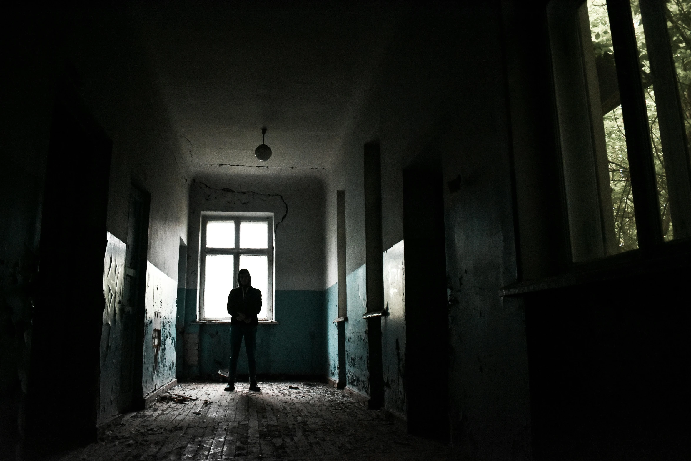 a person standing in a dark hallway next to a window, antipodeans, schools, abandoned, in a room, indoor picture