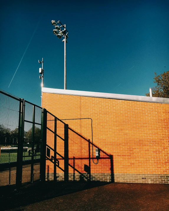 a view of a baseball field from behind a fence, an album cover, by Christen Dalsgaard, unsplash, conceptual art, brick building, transmitters on roof, floodlight, today\'s featured photograph 4k