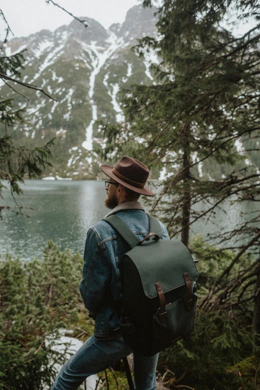 a man with a backpack standing in front of a lake, by Jessie Algie, unsplash contest winner, visual art, in green forest, wearing a travel hat, felix englund style, looking outside