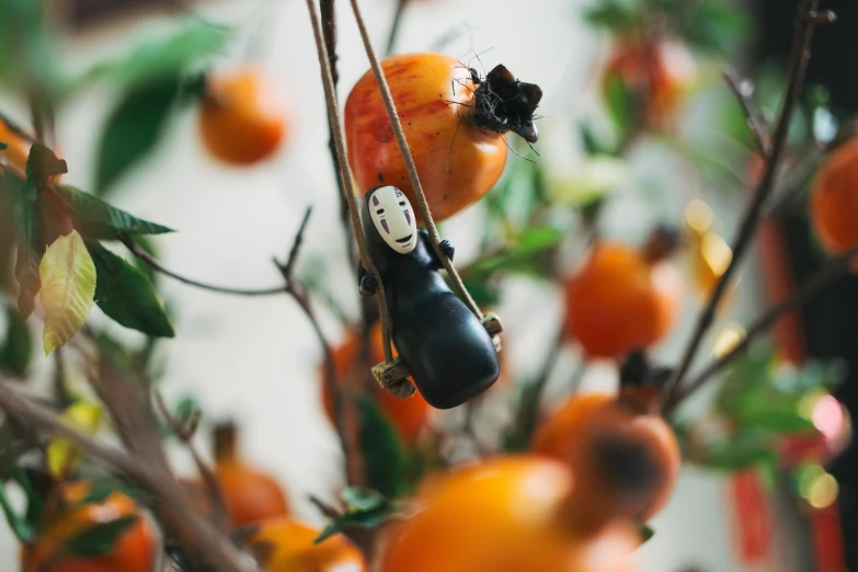 a couple of figurines hanging from a tree, inspired by Studio Ghibli, unsplash, fruit, black and orange, close - shot, gardening