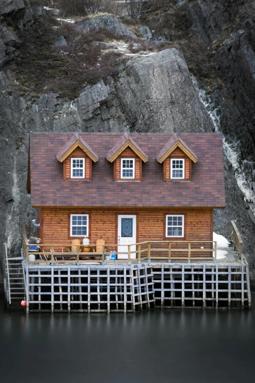 a small wooden house sitting on top of a body of water, rocky cliff, smug look, high-resolution photo, docked at harbor