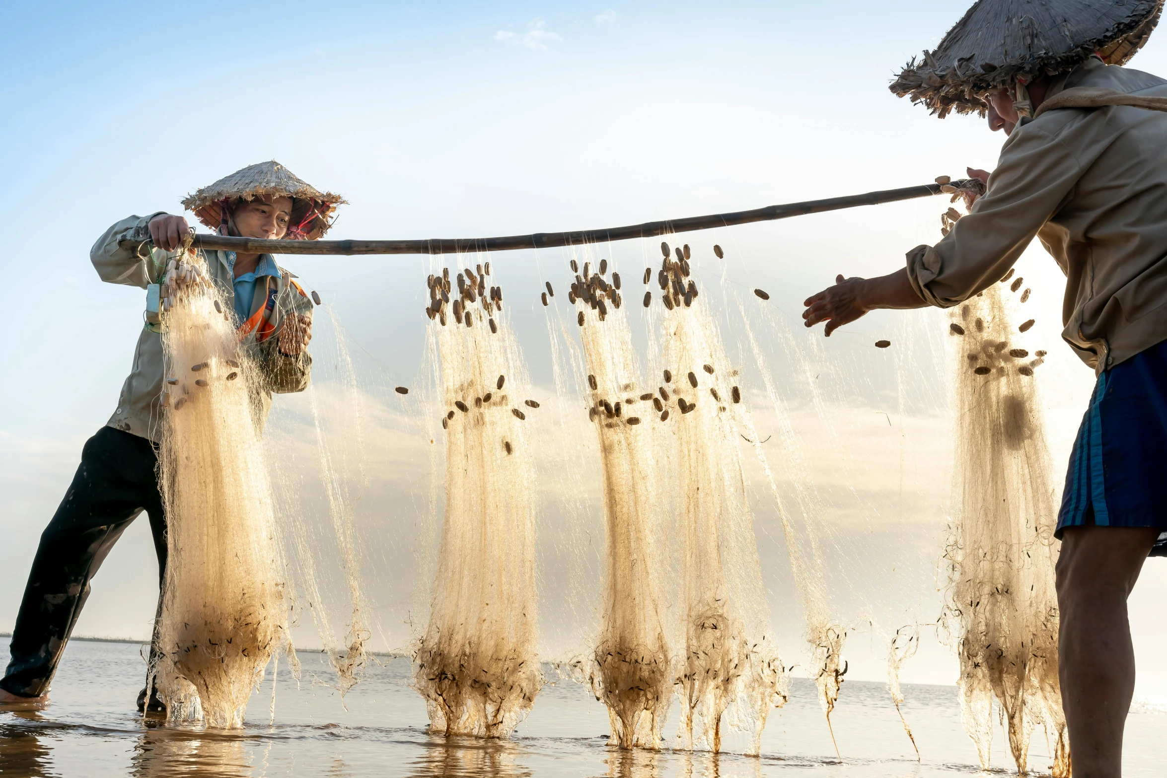 a couple of people standing on top of a beach, inspired by Steve McCurry, unsplash contest winner, process art, fish flocks, nets, traditional chinese clothing, harvest