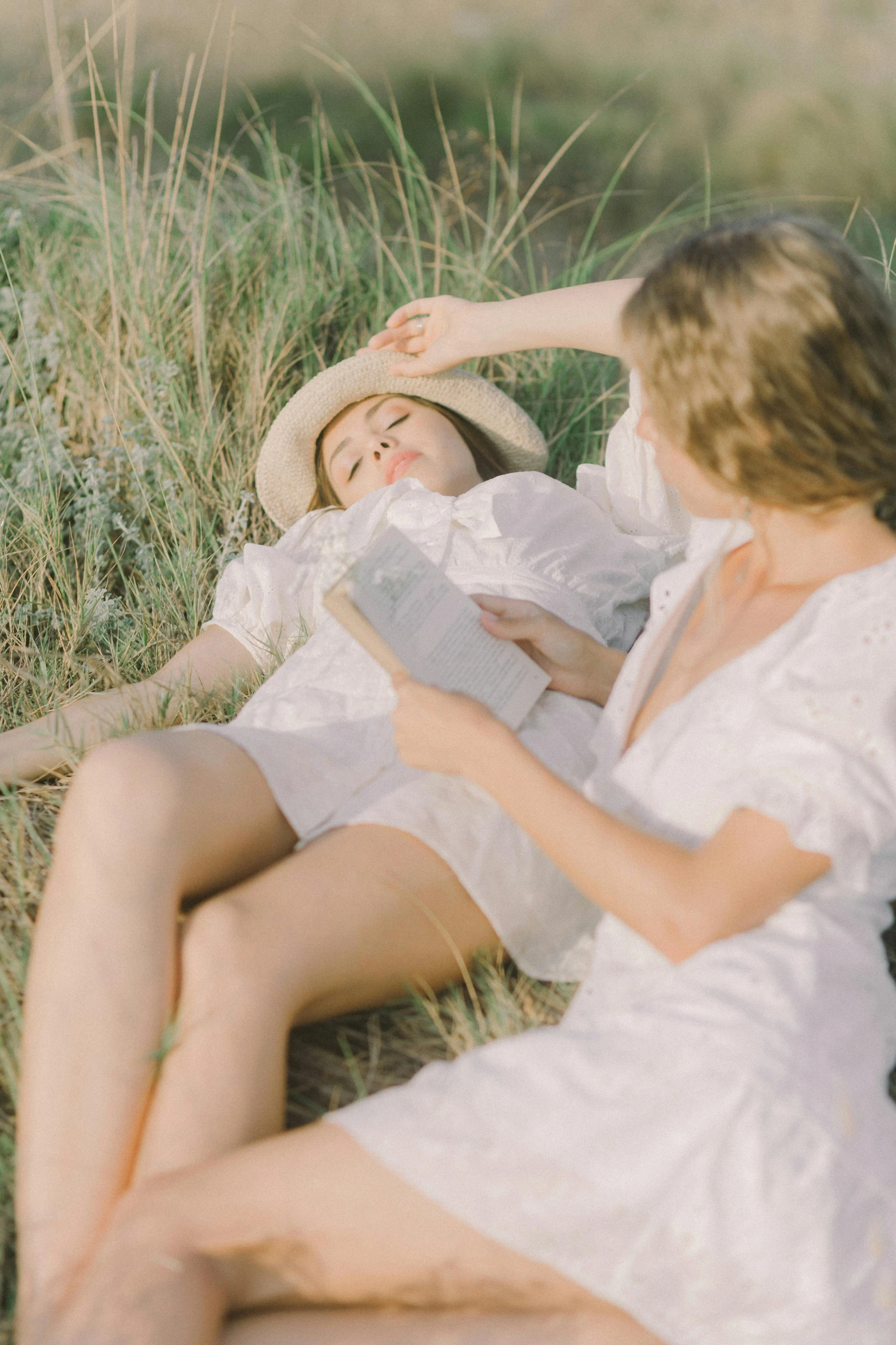 a couple of women laying on top of a grass covered field, inspired by Elsa Bleda, unsplash contest winner, post-impressionism, wearing a cute white dress, reading the book about love, white straw flat brimmed hat, gif