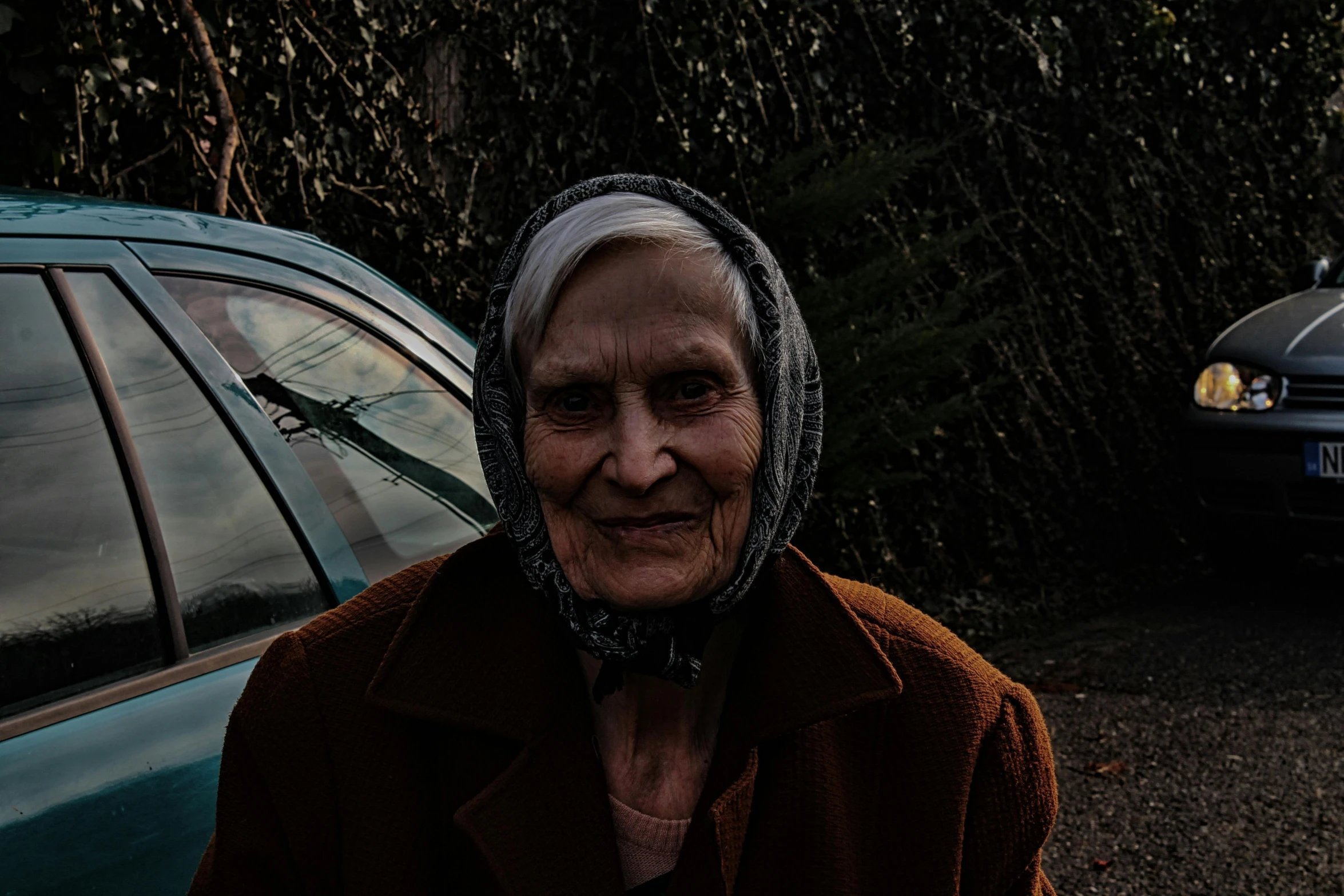 an old woman standing in front of a parked car, an album cover, by Attila Meszlenyi, pexels contest winner, full faced, mother of witchers, late evening, ((portrait))