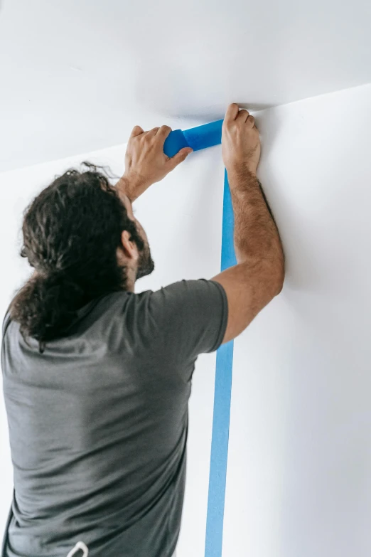 a man painting a wall with a blue tape, trending on reddit, detailed product image, ( ( theatrical ) ), david kassan, hanging