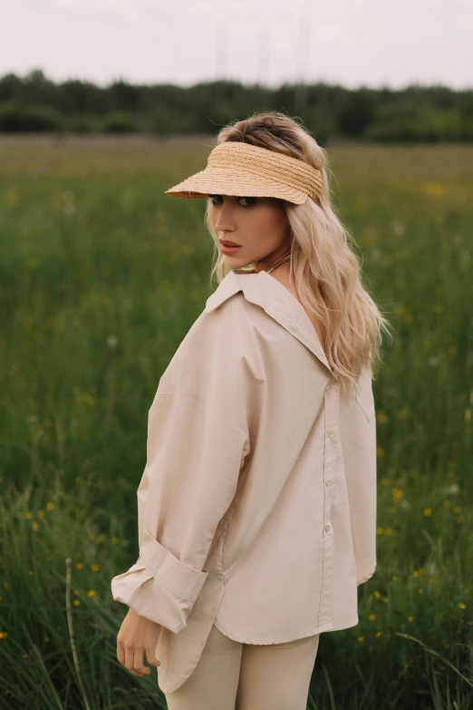 a woman standing in a field wearing a hat, long swept back blond hair, wear's beige shirt, thumbnail, julia sarda