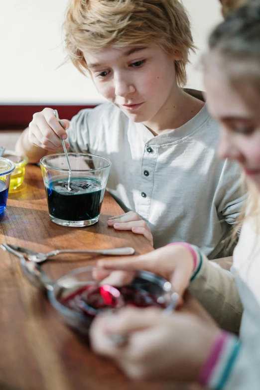 a couple of kids that are sitting at a table, pexels, process art, scientific glassware, newton's cradle, oil slick, breakfast